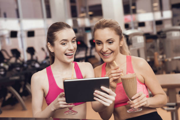 Woman and girl in sportswear drinking protein shakes at the gym. 